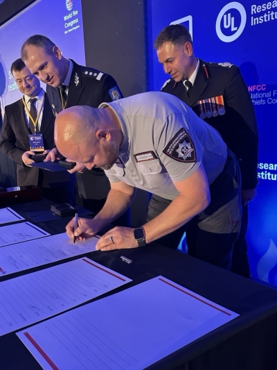 VUGD priekšnieks ģenerālis M. Baltmanis paraksta dokumenti, aiz viņa stāv trīs vīrieši.