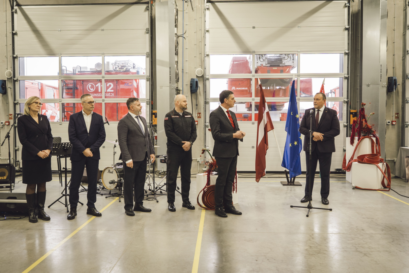 Liepājas katastrofu pārvaldības centra iekštelpa. Uzrunu saka Latvijas Republikas iekšlietu ministrs Rihards Kozlovskis. Citas uzaicinātās amatpersonas nostājušās pa kriesi no viņa.