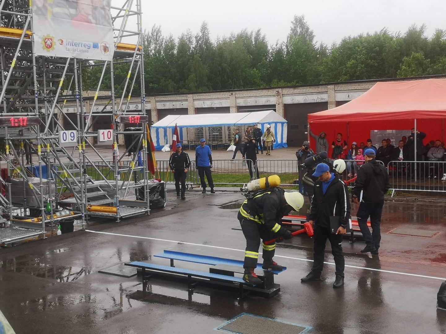 Ugunsdzēsējs glābējs, tērpies pilnā ekipējumā, stāv un sit ar sarkanu āmuru pa metālu
