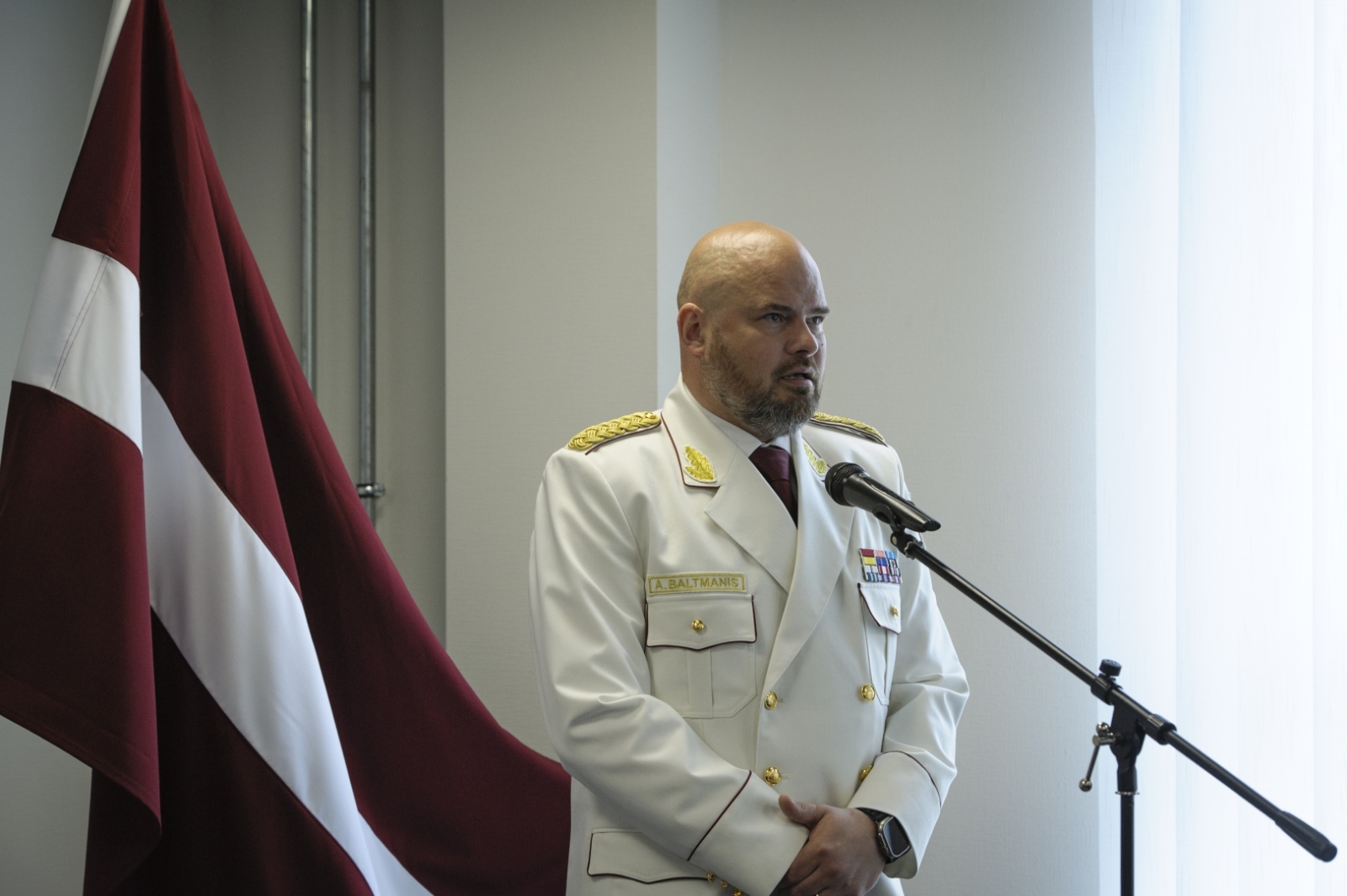 VUGD priekšnieks Mārtiņš Baltmanis saka runu. Aiz viņa kreisajā pusē Latvijas karogs.