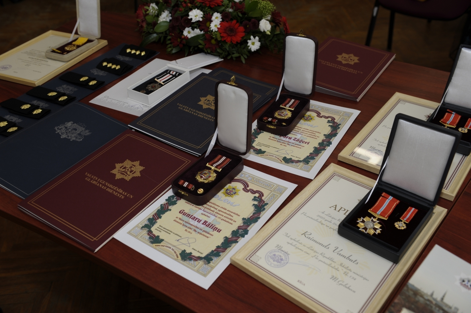 Uz galda stāv novietotas Pateicības, Apliecības, Diplomi, kā arī goda zīmes