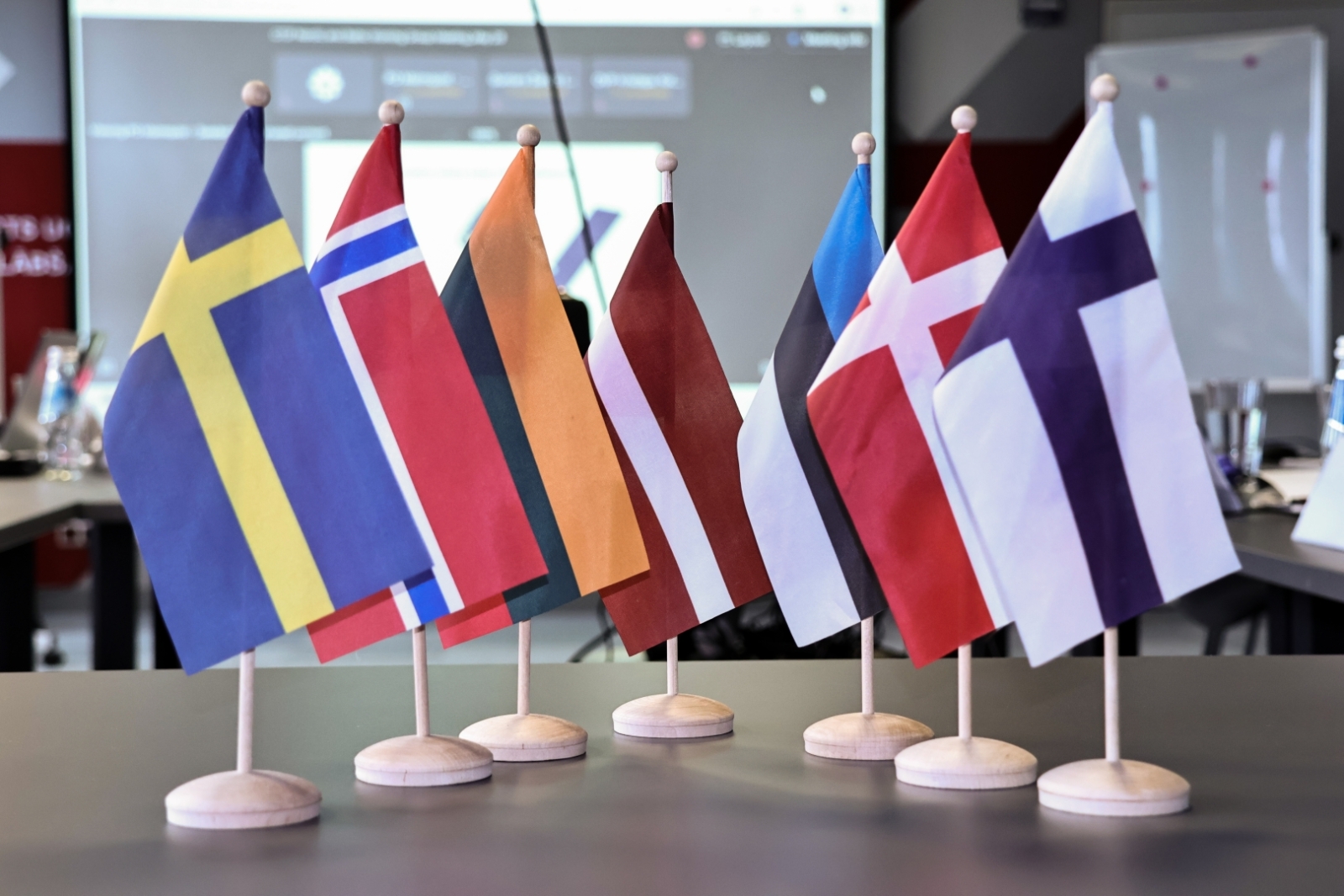 Uz galda izkārtoti karogi - Zviedrijas, Norvēģijas, Lietuvas, Latvijas, Igaunijas, Dānijas un Somijas.