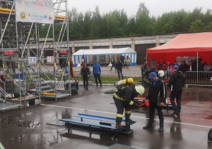 Ugunsdzēsējs glābējs, tērpies pilnā ekipējumā, stāv un sit ar sarkanu āmuru pa metālu