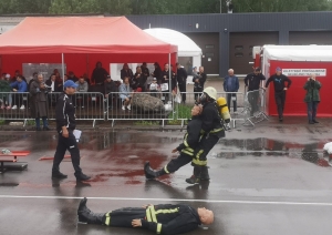 Ugunsdzēsējs glābējs, tērpies pilnā ekipējumā, velk, turot aiz padusēm, manekenu