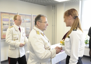 Vīrietis baltā žaketē pasniedz apbalvojumu sievietei