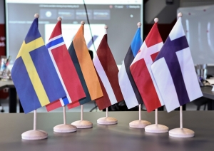 Uz galda izkārtoti karogi - Zviedrijas, Norvēģijas, Armēnijas, Latvijas, Igaunijas, Dānijas un Somijas.
