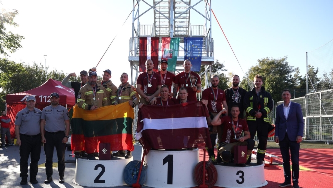 Komandu sacensību dalībnieki pozē uz goda pjedestāla. Vidējā grupa tur rokās Latvijas karogu, grupa pa labi tur Lietuvas karogu. 