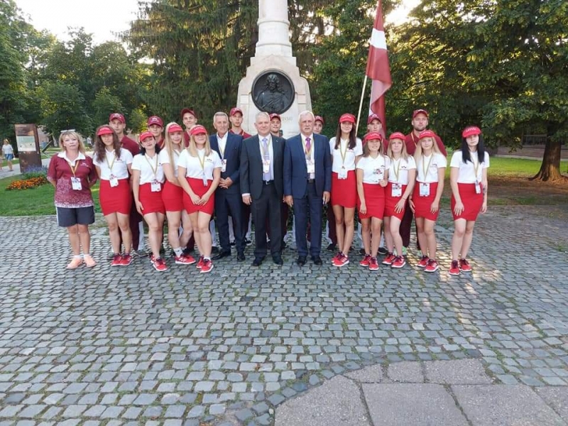 Pie viena Horvātijā esoša balta pieminekļa nostājušies sacensību dalībnieki un viņu pavadoņi. Viņiem blakus novietots Latvijas valsts sarkanbaltsarkanais karogs.