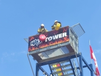 Metāla tornis, kuram augšā atrodas divi ugunsdzēsēji glābēji, kuri katrs velk augšā striķī iekārtu apaļas formas smagumu. Vienam virvē iekārtais smagums ir sarkanā krāsā ar baltu krustu, bet otram - dzeltenā