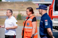 Stāv trīs cilvēki - Valsts ugunsdzēsības un glābšanas dienesta priekšnieka vietnieks, viņam blakus Neatliekamās medicīniskās palīdzības dienesta vadītāja, tērpusies spilgti oranžajā dienesta tērpā, un Valsts policijas pārstāvis, tērpies dienesta zilajā tērpā.