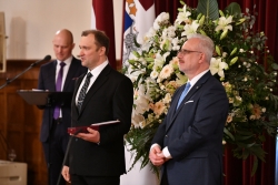 VUGD darbinieks melnā uzvalkā stāv blakus Latvijas valsts prezidentam un tur rokās saņemto apbalvojumu