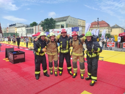 Pieci ugunsdzēsēji glābēji, uzlikuši rokas viens otram uz pleciem, skatās fotogrāfa virzienā. Visi tērpušies savos ugunsdzēsēju glābēju tērpos