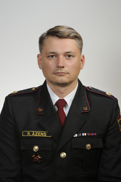 Vīrietis, tērpies tumšas krāsas formastērpā, skatās fotogrāfa virzienā.