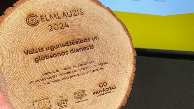 Koka ripa. Tās augšpusē teksts: Celmlauzis 2024. Zem tā iestādes nosaukums - Valsts ugunsdzēsības un glābšanas dienests. Zem iestādes nosaukuma sniegts atšifrējums tam, ko nozīmē apzīmējums - celmlauzis. Koka ripas apakšpusē redzami dažādi logo.