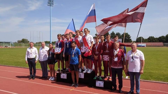 Uz stadiona sarkanīgā skrejceļa novietoti pjedestāli. Uz tiem uzkāpuši sacensību dalībnieki un uzvarētāji. Tiem aiz muguras novietoti trīs valstu karogi.