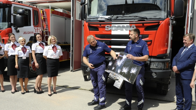 Divi valsts policijas nodarbinātie stāv pie sarkanās autocisternas un tur rokās gleznu - baltas pieneņpūkas uz pelēkas fona. Kreisajā pusē stāv dispečeres, bet labajā iekšlietu ministrs.