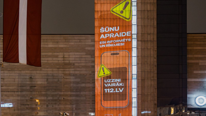 Uz spoguļotas virsmas organžas krāsas Šūnu apraides kampaņas vizuālis ar informāciju par kampaņu