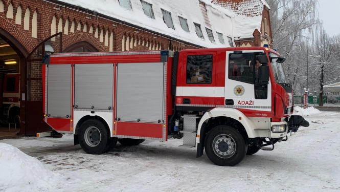 Ugunsdzēsēju glābēju sarkani baltā autocisterna ziemas laikā stāv pie no sarkaniem ķieģeļiem būvēta ugunsdzēsības depo