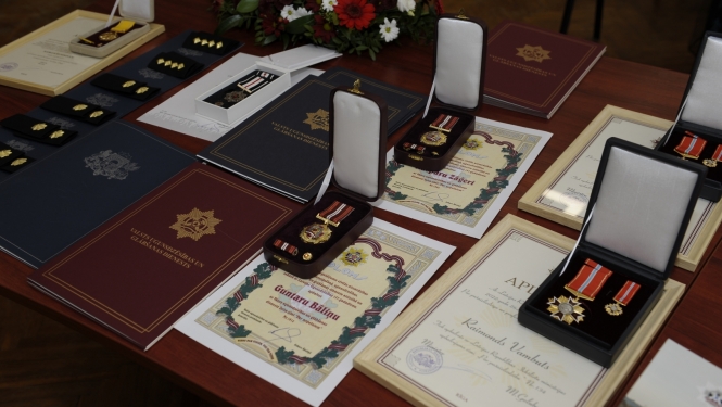 Uz galda stāv novietotas Pateicības, Apliecības, Diplomi, kā arī goda zīmes