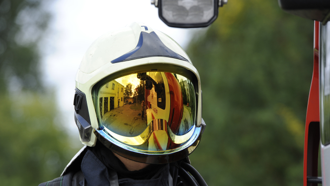 Ugunsdzēsējs glābējs, kurš sev galvā uzvilcis aizsargķiveri. Ķiveres aizsargstikls ir nolaists uz leju, tādējādi aizsedzot ugunsdzēsēja glābēja seju.