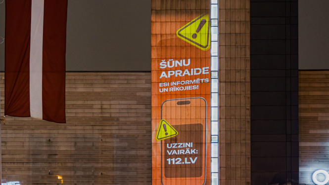 Uz spoguļotas virsmas organžas krāsas Šūnu apraides kampaņas vizuālis ar informāciju par kampaņu