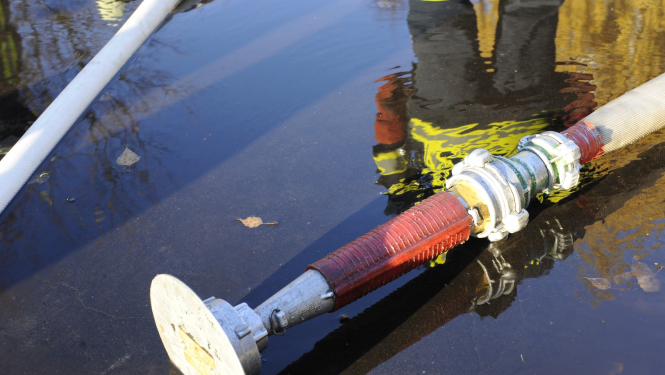 Peļķē stāv viens no ugunsdzēsēju glābēju aprīkojuma elementiem. Peļķes atspulgā redzams ugunsdzēsējs glābējs