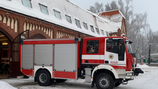 Ugunsdzēsēju glābēju sarkani baltā autocisterna ziemas laikā stāv pie no sarkaniem ķieģeļiem būvēta ugunsdzēsības depo