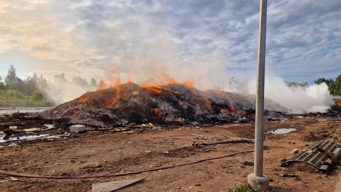 Uz brūnas zemes atrodas melna degošu atkritumu kaudze. No tās ceļas dūmi. Fonā zilganas debesis ar tumšiem mākoņiem