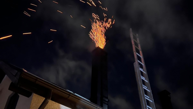 Naktī no mājas skursteņa ārā nāk degoši sodrēji - oranžu dzirksteļu strūklas formā. Pie gaišās mājas atstutētas pelēkas metāla kāpnes.