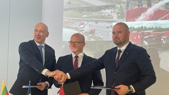 Trīs vīrieši stāv pie galda. Uz galda novietoti Lietuvas, Igaunijas un Latvijas karodziņi. Vīrieši salikuši vienu virs otras savas labās rokas