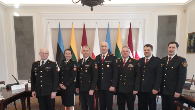 Septiņi konferences dalībnieki, tērpušies savās dienestu formās, stāv pie konferences dalībvalstu karogiem un skatās fotogrāfa virzienā