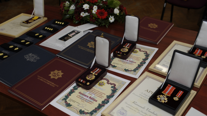 Uz galda stāv novietotas Pateicības, Apliecības, Diplomi, kā arī goda zīmes