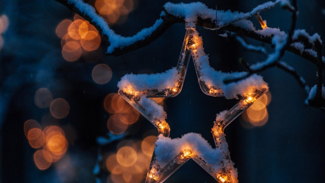 Eglē iekārts nedaudz apsnidzis svētku rotājums - plastmasas zvaigznītes kontūra, kurai iekšā ir pāris degošas lampiņas.