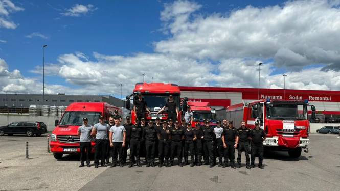 Uz ceļa novietoti četri dažādi Valsts ugunsdzēsības un glābšanas dienesta operatīvie transportlīdzekļi. To priekšā nostājušies mācību dalībnieki.