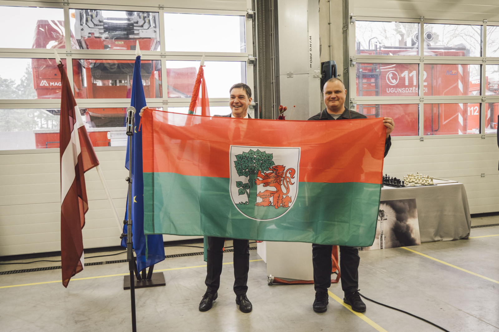 Liepājas mērs Gunārs Ansiņš un Valsts ugundzēsības un glābšanas dienesta nodarbinātais tur Liepājas karogu.