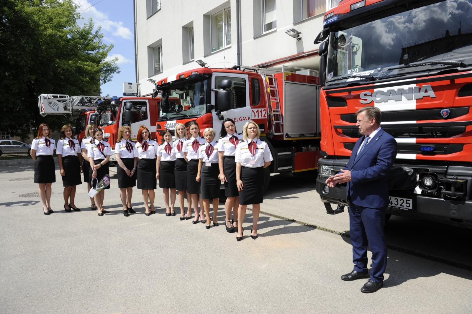 Iekšlietu ministrs saka uzrunu. Viņam aiz muguras atrodas sarkanā autocisterna, bet kreisajā malā 112 zvanu centra dispečeres