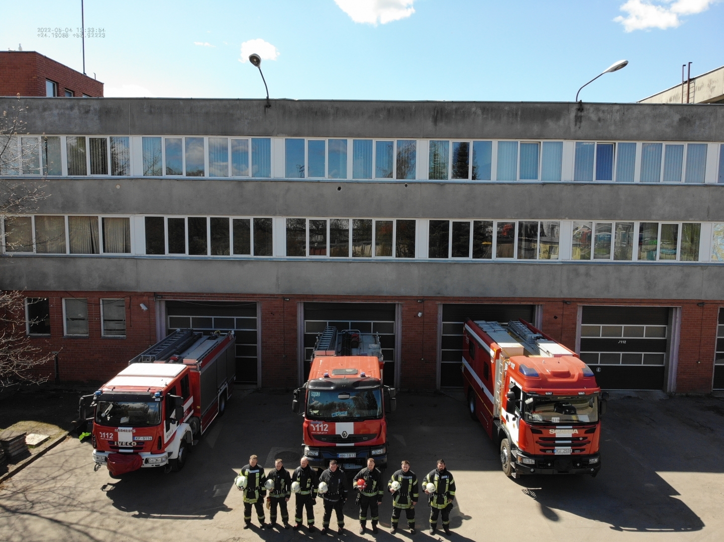 Septiņi ugunsdzēsēji glābēji stāv pie trīs dažādām ugunsdzēsēju glābšanas autotehnikām, ietur klusuma brīdi un rokās tur savas ķiveres