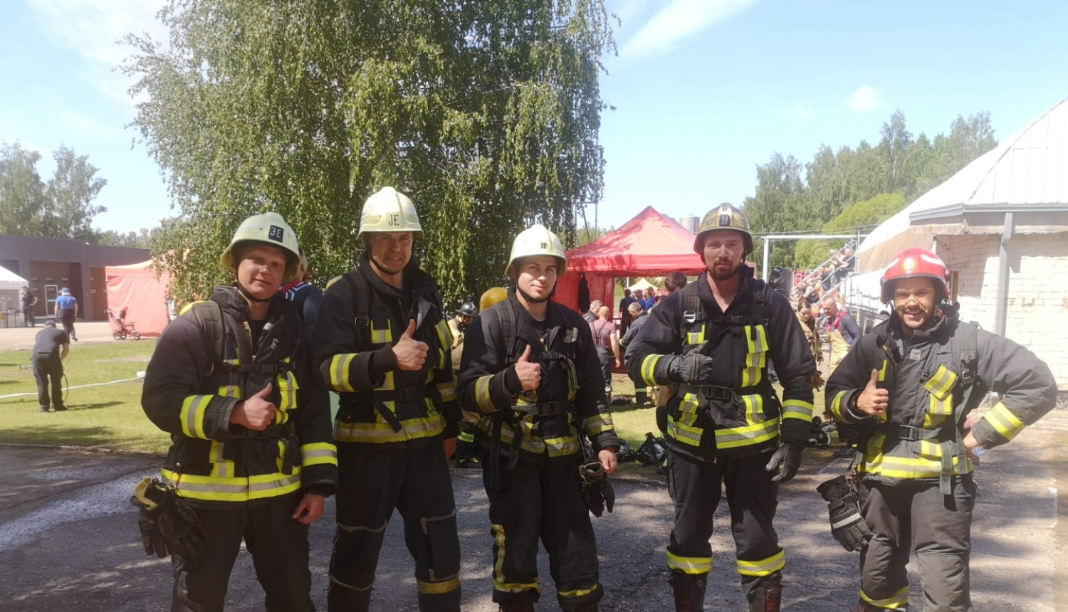 Pieci ugunsdzēsēji glābēji stāv ietērpušies savos formas tērpos un skatās fotogrāfa virzienā