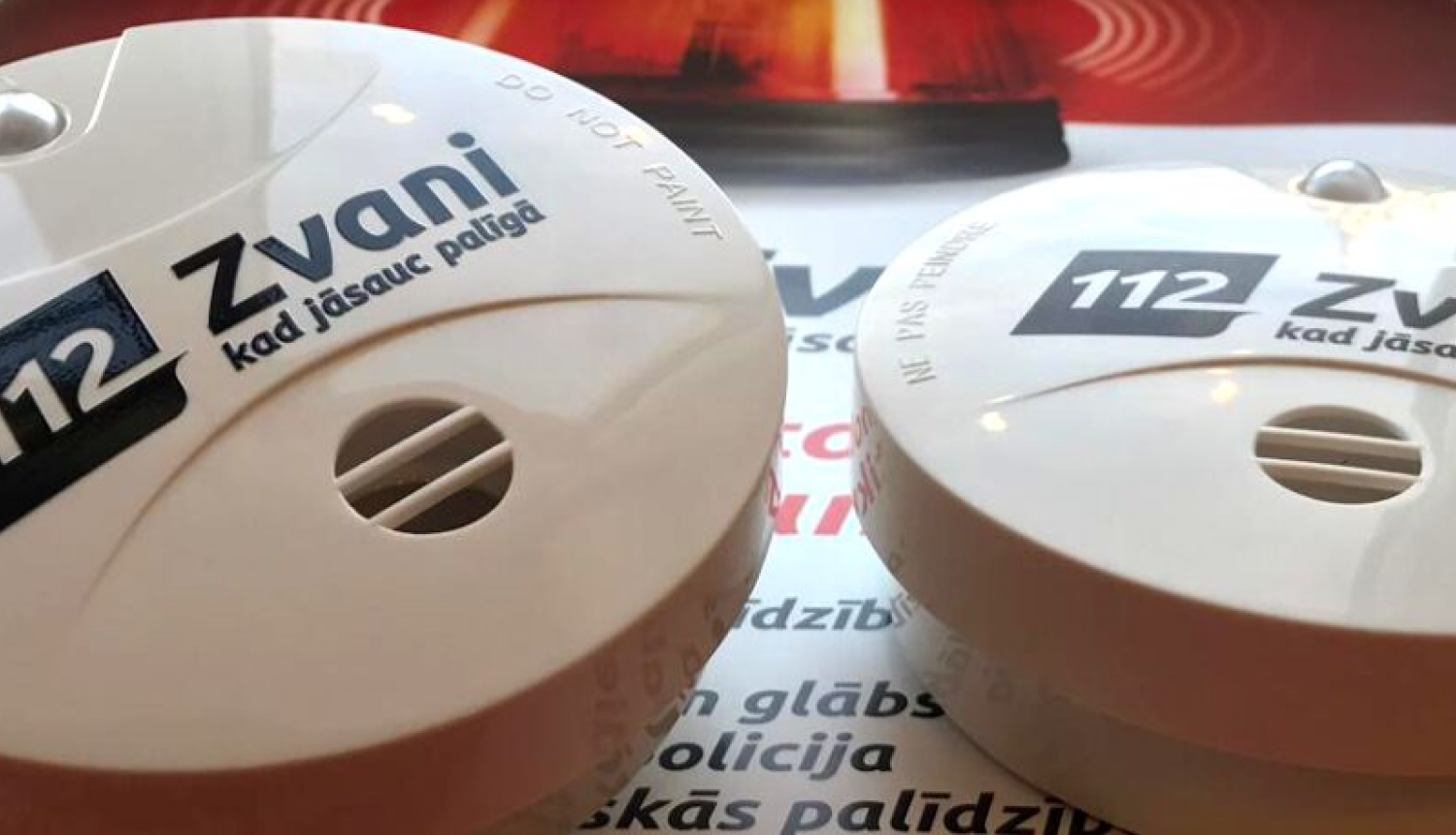 Uz skrejlapas novietoti divi balti dūmu detektori ar vienotā ārkārtas palīdzības izsaukumu numura 112 melno logo - 112 Zvani, kad jāsauc palīgā!