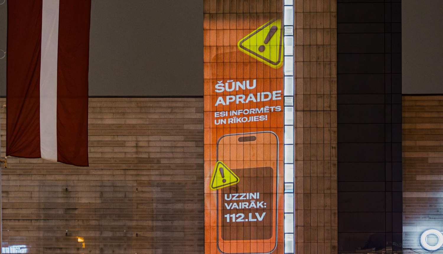 Uz spoguļotas virsmas organžas krāsas Šūnu apraides kampaņas vizuālis ar informāciju par kampaņu