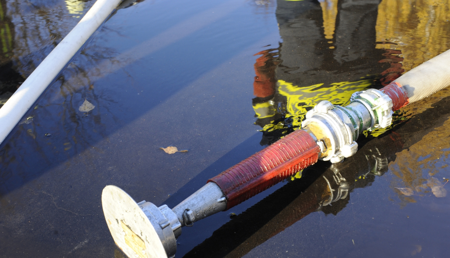 Peļķē stāv viens no ugunsdzēsēju glābēju aprīkojuma elementiem. Peļķes atspulgā redzams ugunsdzēsējs glābējs