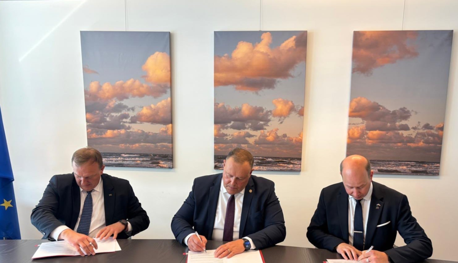 Pie brūna galda sēž trīs uzvalkos tērpušies vīrieši. Visi vīrieši paraksta sev priekšā novietotos dokumentus. Aiz viņu mugurām pie gaišas sienas piestiprinātas trīs atsevišķas gleznas, kas savstarpēji veido skatu uz mākoņainām debesīm.