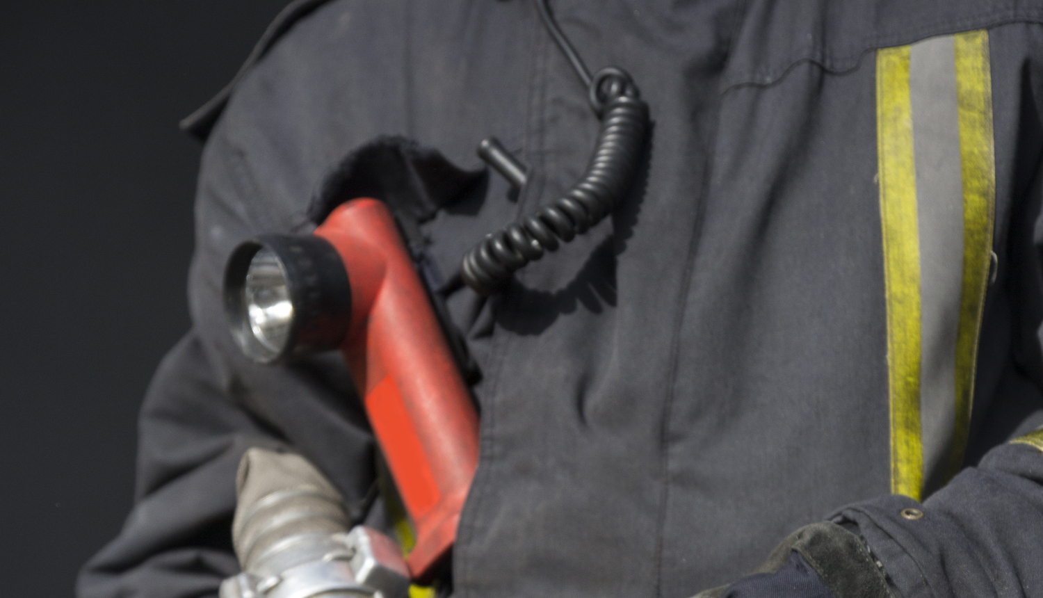 Ugunsdzēsējs glābējs, tērpies aizsargdrēbēs, tur rokās ūdens šļūtenes stobru.