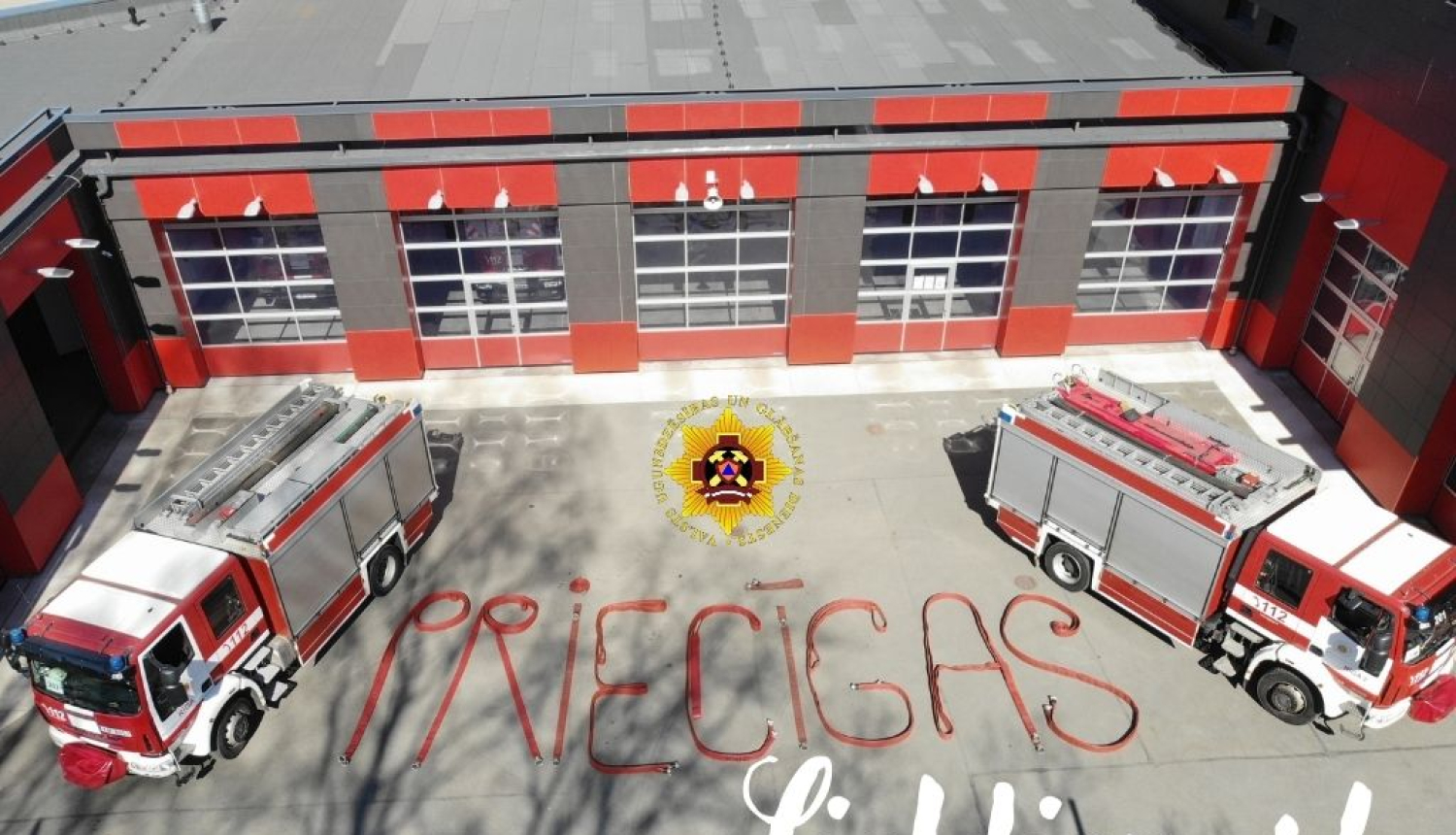 Apsveikums Lieldienās. Tajā redzamas divas ugunsdzēsēju glābēju mašīnas. Mašīnām pa vidu uz zemes ar šļūtenēm izveidots vārds - Priecīgas. Klāt pierakstīts vārds Lieldienas!