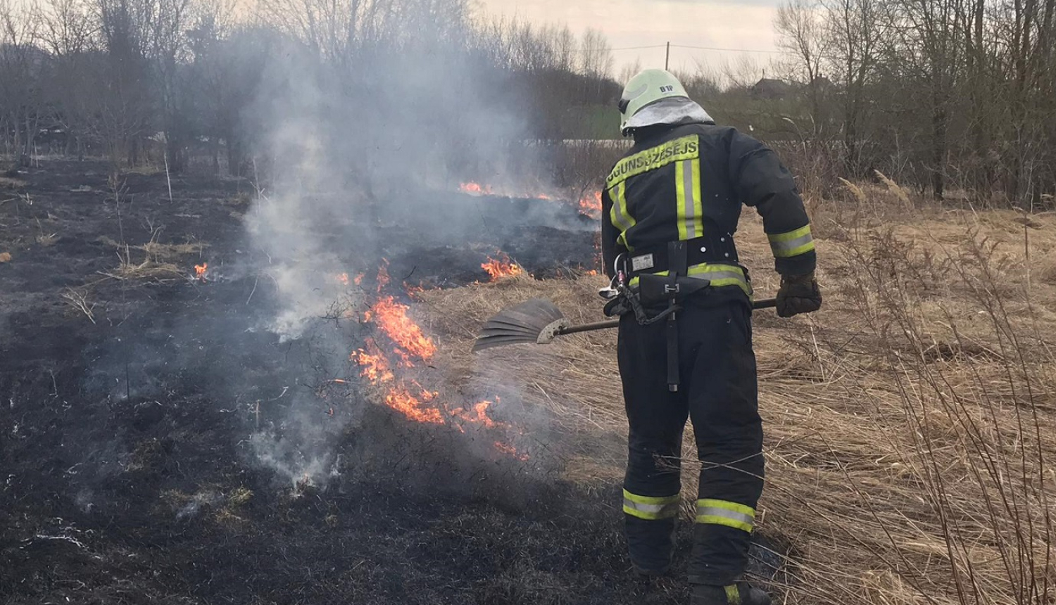 Ugunsdzēsējs glābējs ar pletni dzēš kūlas ugunsgrēku.