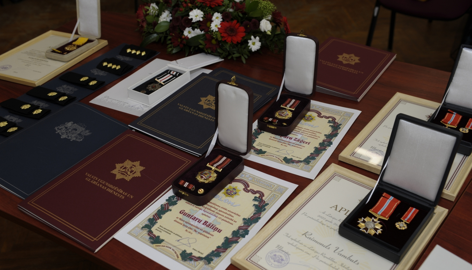 Uz galda stāv novietotas Pateicības, Apliecības, Diplomi, kā arī goda zīmes