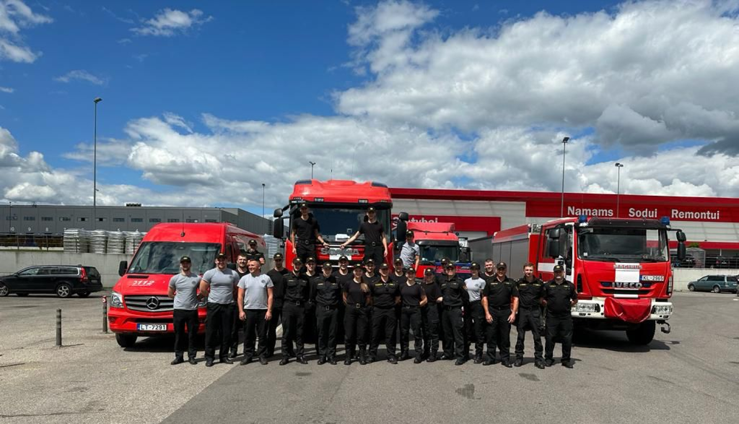 Uz ceļa novietoti četri dažādi Valsts ugunsdzēsības un glābšanas dienesta operatīvie transportlīdzekļi. To priekšā nostājušies mācību dalībnieki.