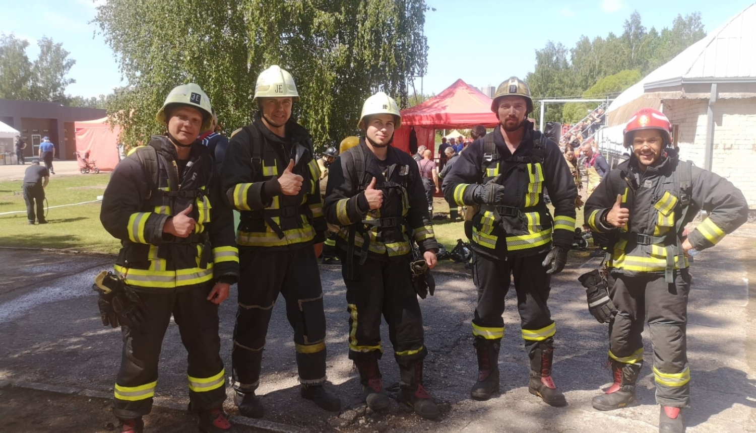 Pieci ugunsdzēsēji glābēji stāv ietērpušies savos formas tērpos un skatās fotogrāfa virzienā