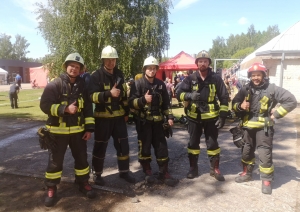 Pieci ugunsdzēsēji glābēji stāv ietērpušies savos formas tērpos un skatās fotogrāfa virzienā